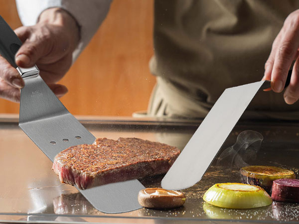 Metal spatulas being used to lift and serve colorful desserts or pastries from a wooden surface.