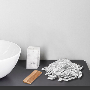 Kitchen cleaning set on dark surface. White bowl, wooden brush, white rectangular object, and pile of white cloths or sponges.