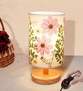 Cylindrical table lamp with pink and white floral pattern on shade, mounted on wooden base with brass fitting, shown with decorative accessories nearby.