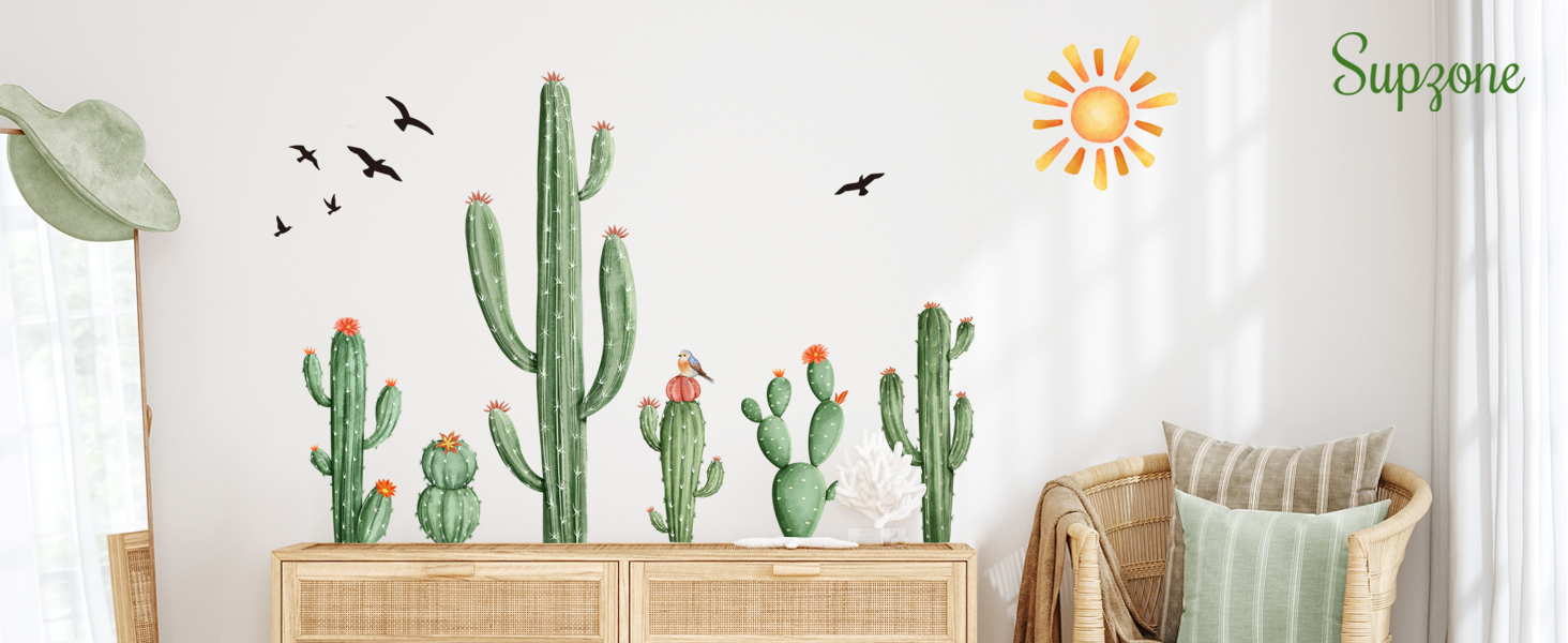Wall decals featuring various cactus designs, birds, and a sun, displayed above a wooden cabinet. A chair with pillows is partially visible in the corner.