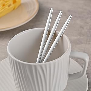 White ceramic ribbed mug containing three metal straws, photographed against light gray surface.