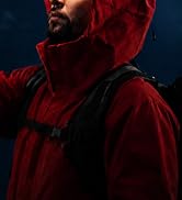 Person wearing red and black waterproof outdoor jacket with hood pulled up against dark blue background. Heavy-duty winter apparel photographed in dramatic lighting showcasing hood design and layered fabric construction.