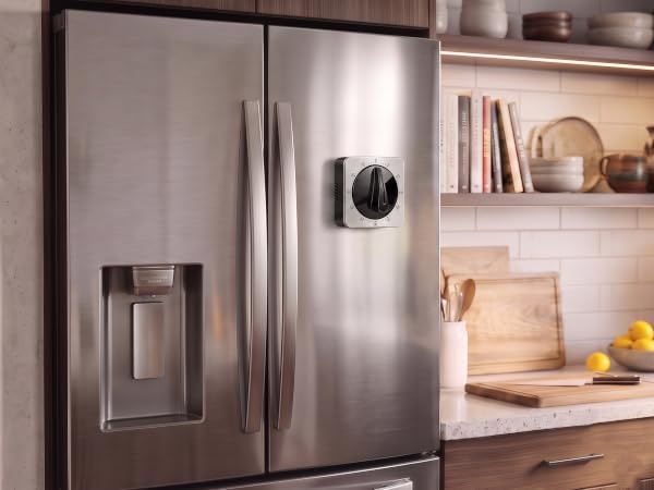 Square mechanical kitchen timer on a refrigerator door in a kitchen.