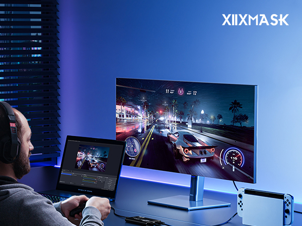 Curved gaming monitor displaying night racing scene, with person using tablet for streaming. Setup includes gaming console and keyboard in blue-lit room.