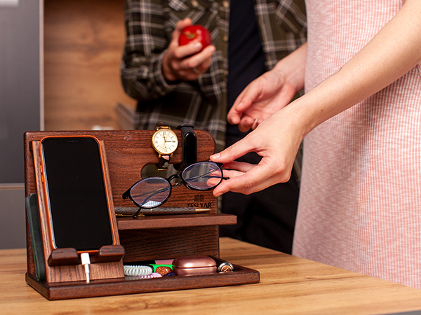 Wooden desk organizer with phone stand, holding glasses, watch, and other small items. Hand placing or removing glasses from the organizer.