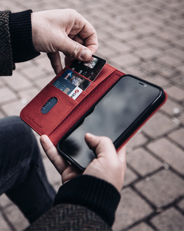 Hands holding a smartphone in a red wallet case, inserting a card into a card slot. The wallet case is open, revealing multiple card slots.