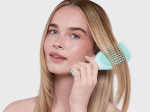 A woman brushing her hair with a blue ultimate detangler brush.