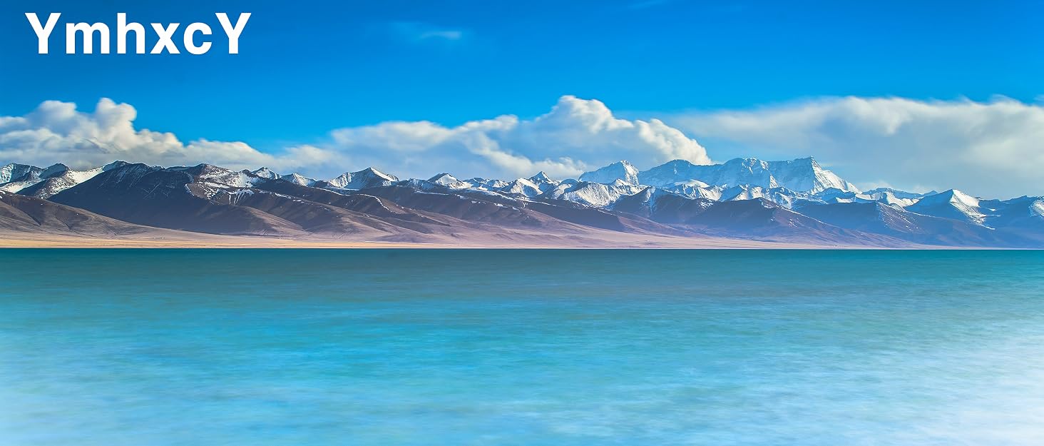 Scenic landscape showing snow-capped mountains behind a turquoise lake or sea under blue skies with white clouds.