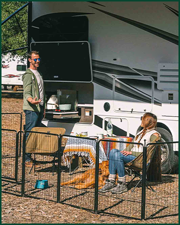 Outdoor scene showing recreational vehicle and portable pet fence enclosure set up in camping or event setting.