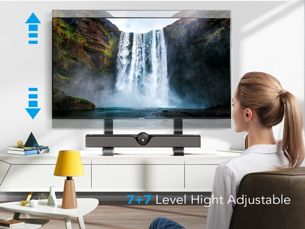 Text reads 'F27 Level Hight Adjustable'. Monitor stand with wooden legs supporting flat-screen television displaying waterfall landscape, person seated at desk with yellow cup visible.