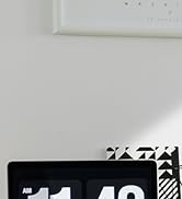 Close-up of a black digital device with a segmented display, positioned on a white surface near a wall.