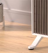 White plastic draft excluder installed at the base of a door, sitting on light wooden flooring. Vertical radiator visible to the right.