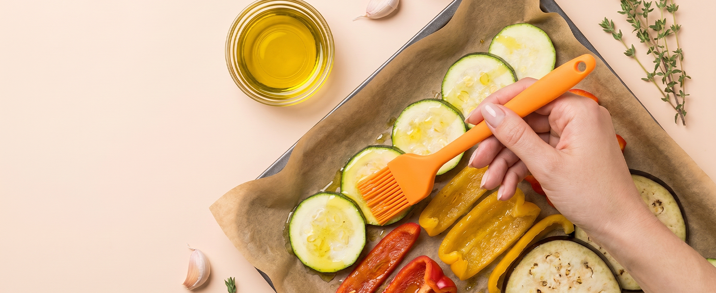 Orange silicone oil brush coating vegetables with olive oil before roasting on peach background