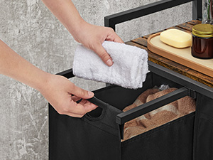 Hands opening a black drawer containing kitchen towels. Wooden cutting board with bread and jar visible on countertop above.