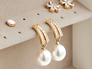Gold-toned earrings with pearl drop pendants and crystal-studded curved design, displayed on beige surface with matching studs.