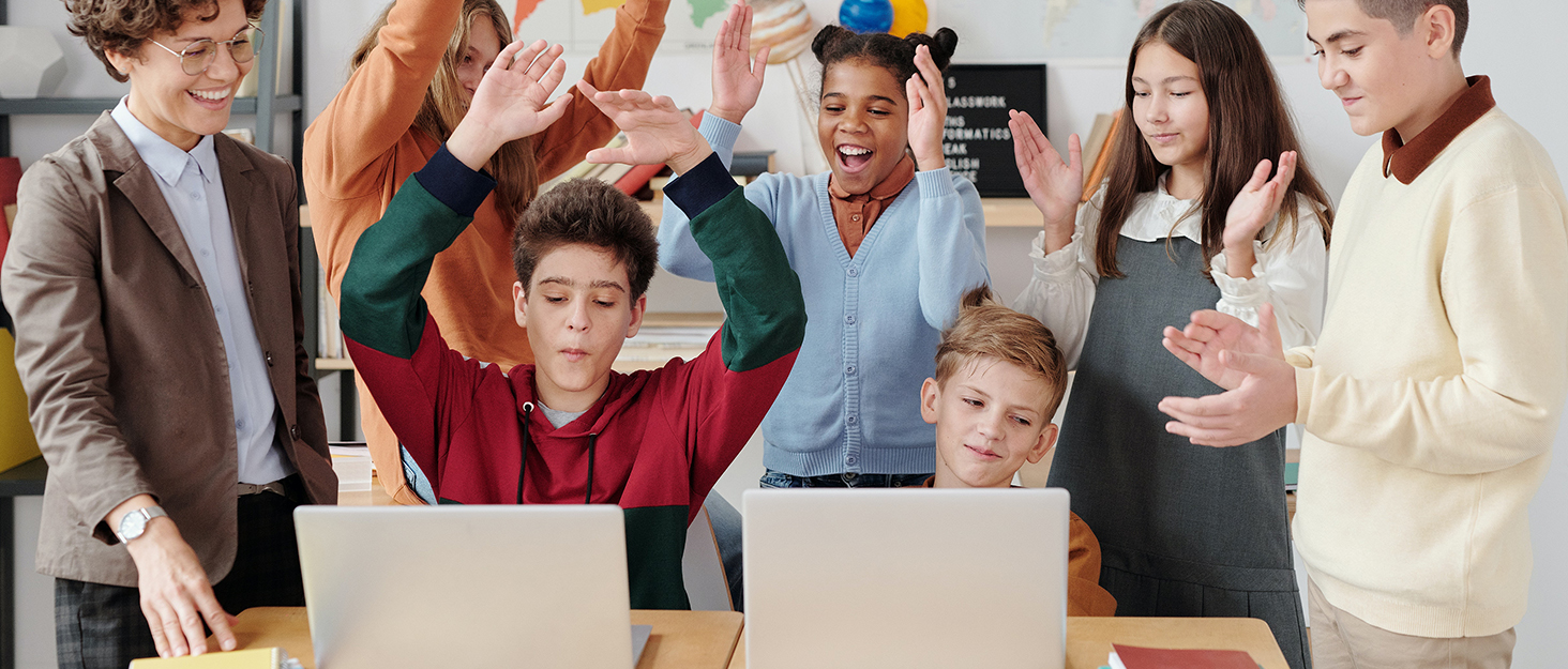 Group gathered around laptops in an animated discussion, showing various expressions of engagement and interaction in what appears to be a collaborative setting.