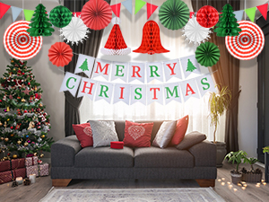 Christmas decorations in living room. 'Merry Christmas' banner, paper fans, tree, and wreath visible. Couch with festive pillows.