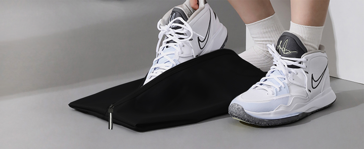 White Nike basketball shoes with gray soles worn on feet. One foot rests on a black mat or surface, demonstrating the shoe's flexibility and fit.