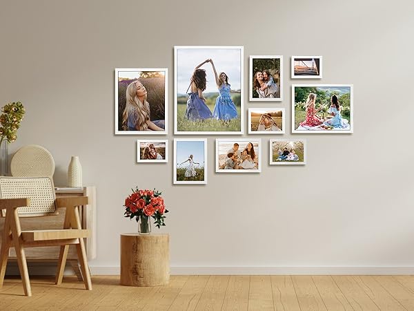 Gallery wall arrangement featuring multiple white-framed photographs arranged asymmetrically on beige wall, with decorative vase and armchair below.