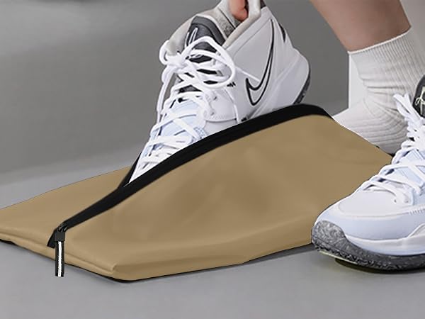 White Nike basketball shoes with black swoosh logo, worn on feet. Beside them is a folded beige fabric, possibly a bag or cover, with black zipper.