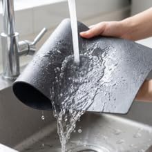 Black PU leather coffee mat rinsed under faucet, showing waterproof easy-clean surface.