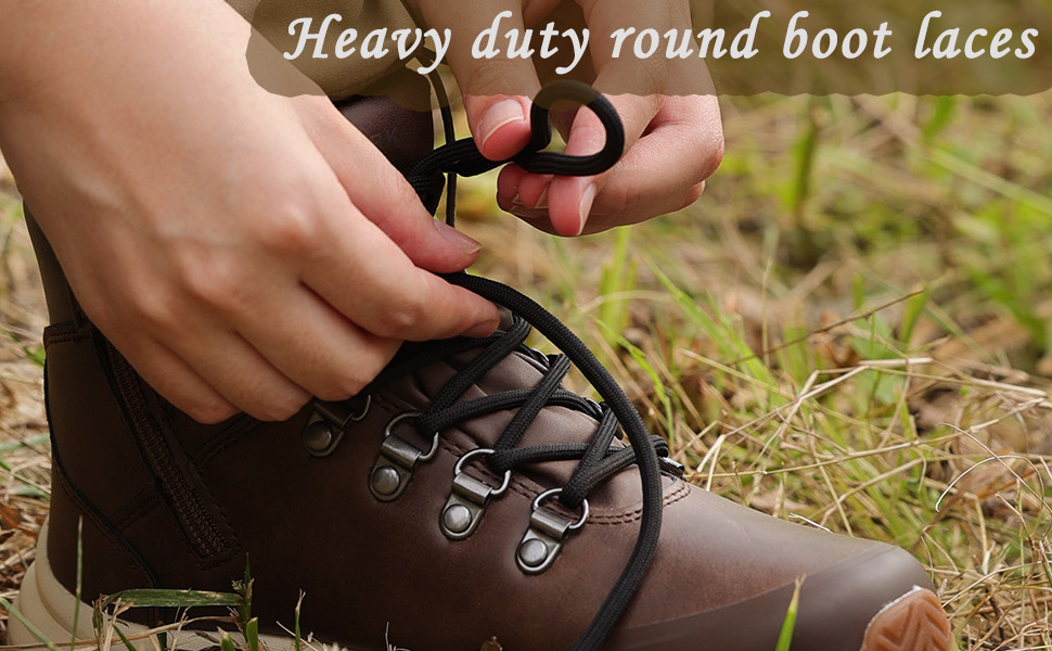 Close-up of hands lacing heavy-duty round boot laces through metal eyelets on a brown leather hiking boot. Outdoor grass setting visible.