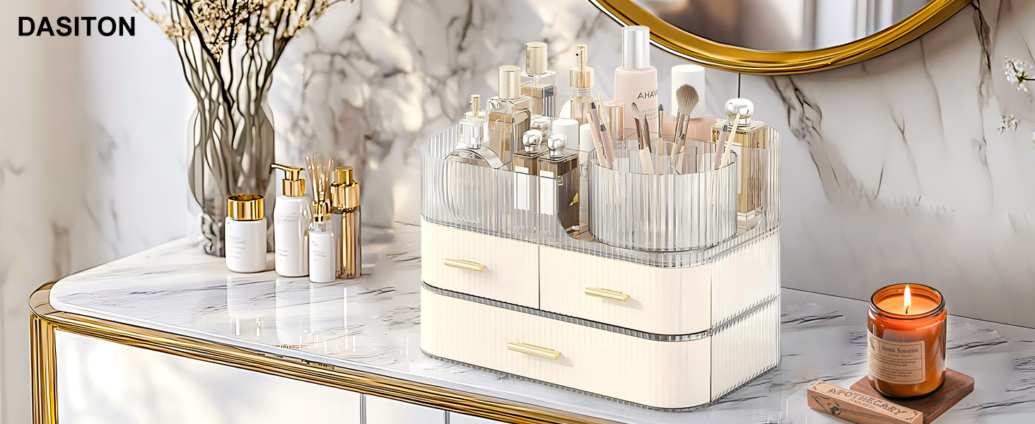 Clear makeup brush holder with gold accents on a marble surface. Contains various white and gold makeup brushes. Nearby are decorative items and a candle.