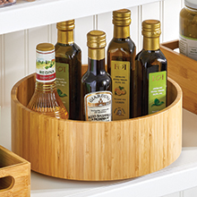 natural bamboo turntable bin holding kitchen oils on white shelf with white paneling in background