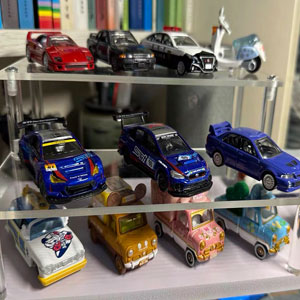 Display of toy or model vehicles arranged on shelves, predominantly blue-colored racing or sports cars in multiple rows.