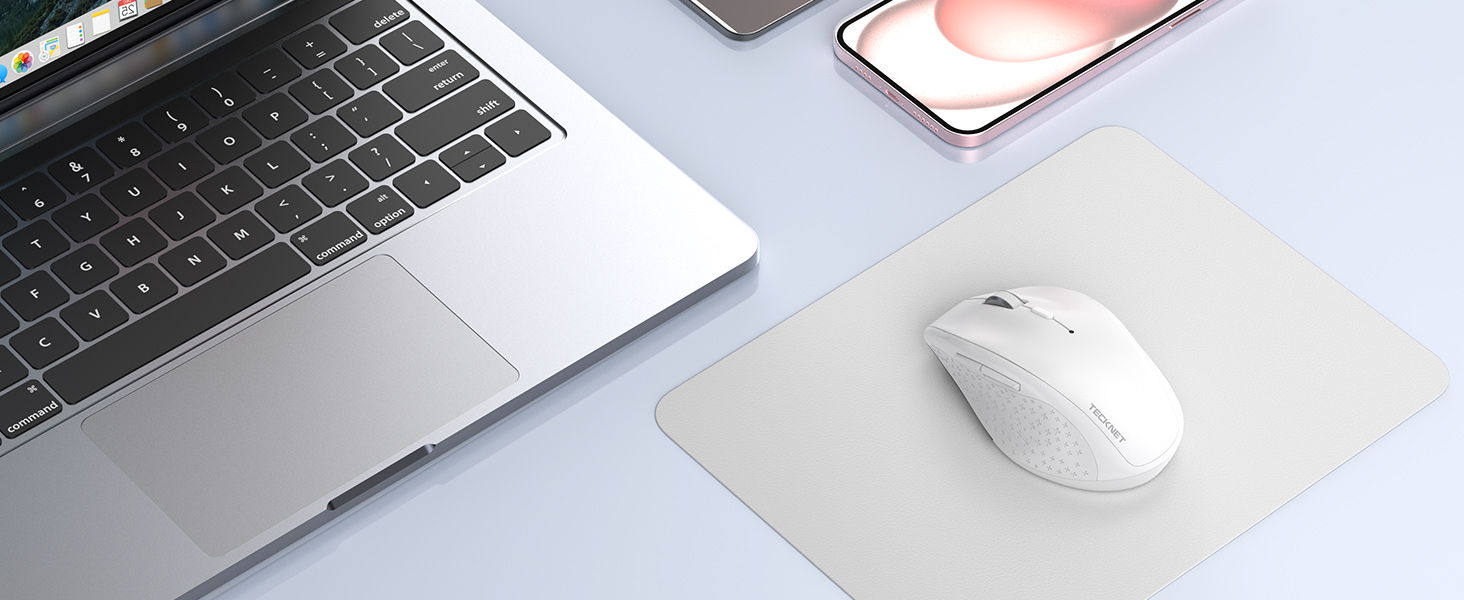 White wireless computer mouse positioned next to a laptop corner and smartphone on light gray surface.