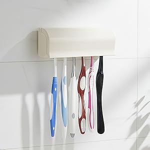 White wall-mounted organizer with cream-colored top rail holding multiple hanging toothbrushes in blue, red, black, and other colors with clear spacing between each brush.