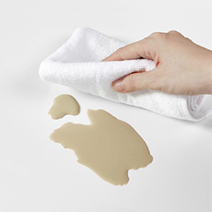 a hand wiping a coffee stain on a white surface.