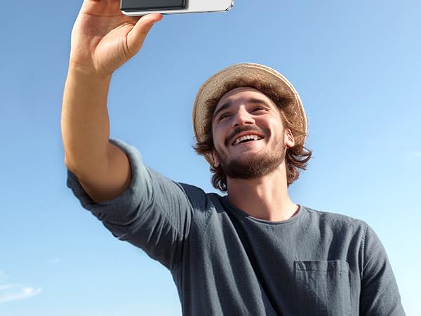Person wearing a gray t-shirt and beanie hat holding up something against a bright blue sky background.