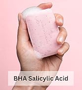 Text reads 'BHA Salicylic Acid'. Hand holding pink solid skincare product against pink background.