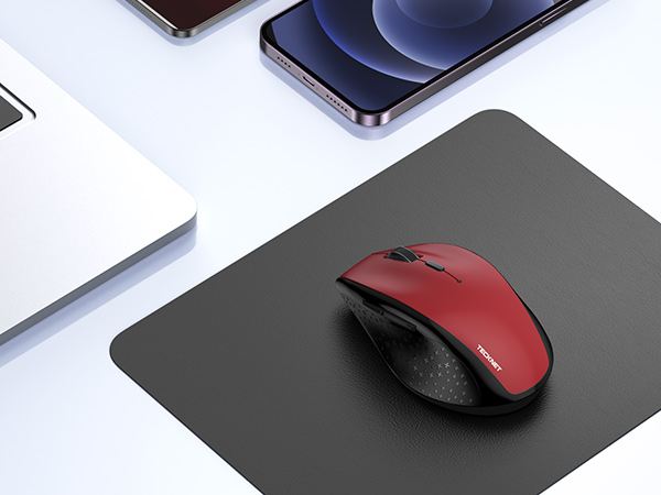 Red wireless computer mouse on dark mousepad, with smartphones and tablets in background on white surface.
