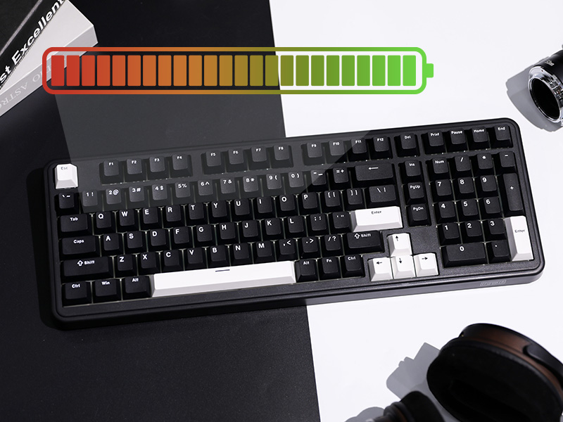 Black computer keyboard with white keys on a split black and white background. Colorful battery icon above. Partial views of other devices visible.