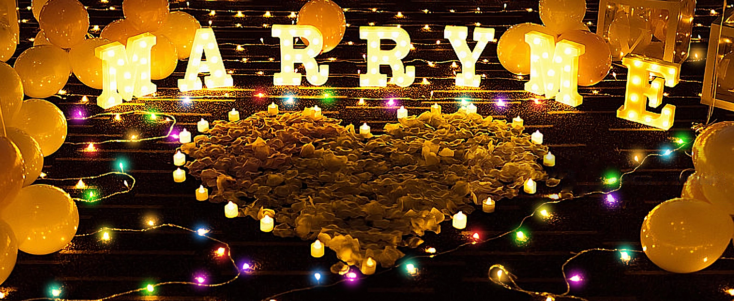 Illuminated 'MARRY' text display with golden balloons and multicolored string lights against dark background.