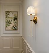 Elegant interior hallway featuring white wainscoting, hardwood floors, and wall sconces. Natural light streams through windows, highlighting traditional architectural details.