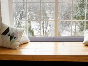 Interior scene showing a wooden windowsill or shelf with decorative items against a bright window with trees visible outside.
