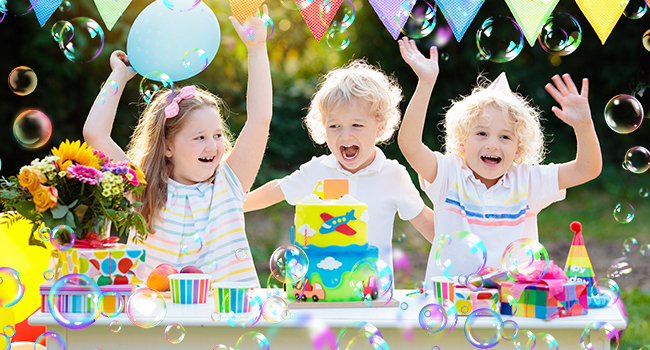Festive birthday party scene with colorful decorations, bubbles floating, and birthday cakes on a table with bright party supplies.