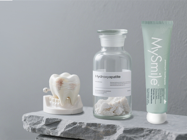 Minimalist product photography showing white cosmetic containers and jars arranged on gray stone surface against light background. Includes frosted glass containers and cream-colored vessels.
