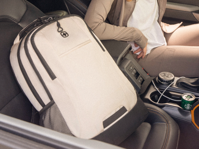 Person placing a cream laptop backpack onto a car seat using the top carry handle