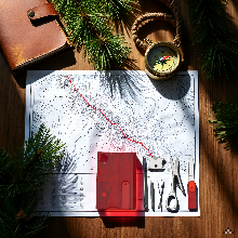 A rugged wooden campsite table with scattered pine cones, a folded map, and soft lantern light glowi