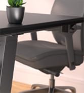 Corner of a dark desk or table with a small potted succulent plant in a black container. Part of an office chair visible underneath.