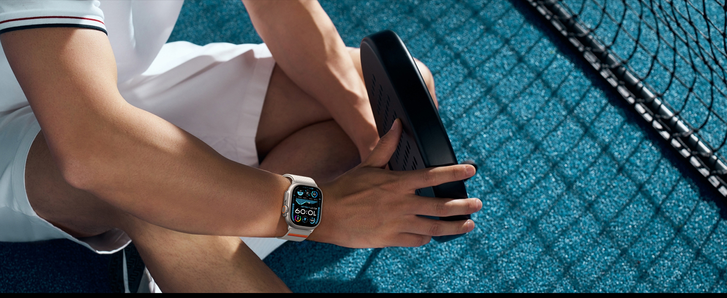 Person wearing a rectangular smartwatch with digital display, sitting on a blue textured surface. The watch face shows time and fitness data.