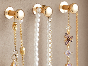 Three gold-toned wall hooks with decorative chains and charms hanging from them. Hooks have a round white center and gold outer rim.