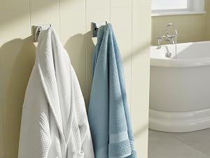 Modern bathroom interior featuring a freestanding white bathtub, beige walls, and hanging blue and white towels on wall-mounted racks.