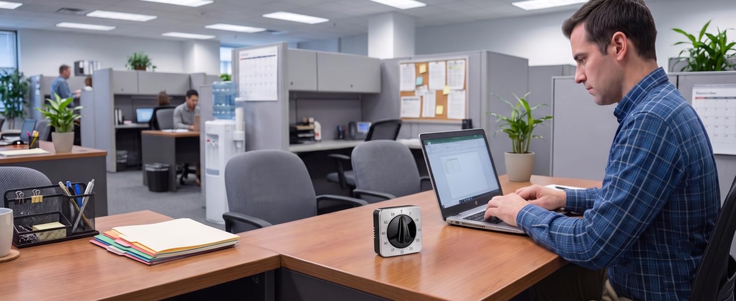 mechanical timer on an office desk next to a man using a laptop