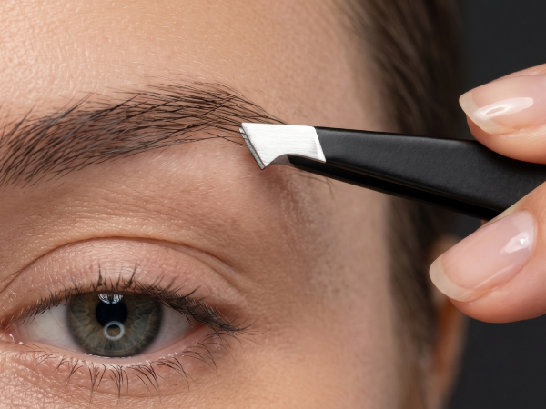 Close-up of eyebrow application tool with black handle being used on a person's eyebrow to shape and define the brow area.
