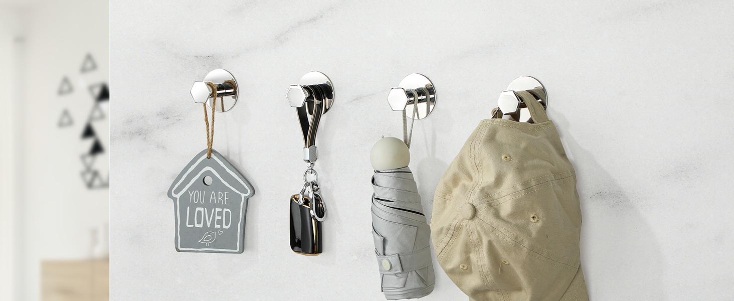 Row of decorative wall hooks displaying various items including a house-shaped ornament, bottles, and textured objects against white wall.